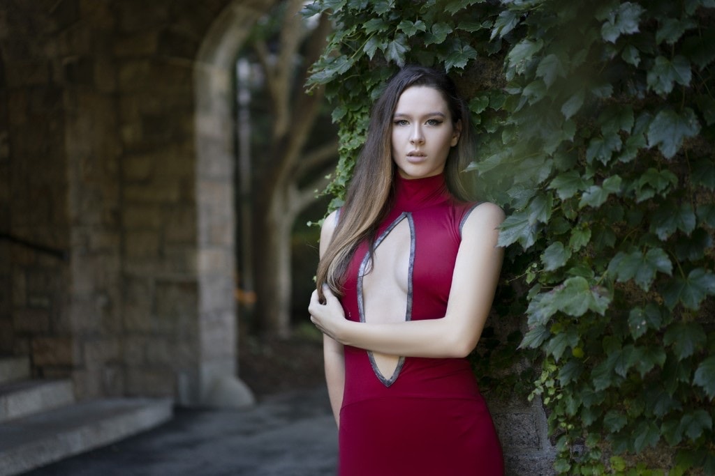 Woman in a red dress leaning against a stone wall covered in ivy