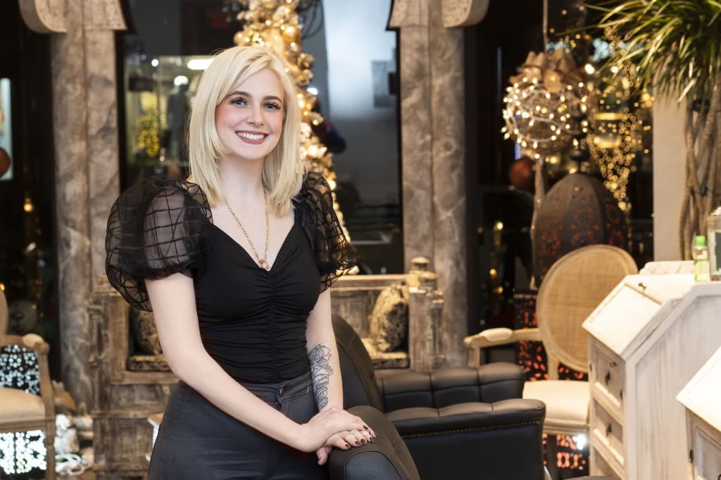 Smiling woman with a blonde bob seated in a salon decorated for the holidays